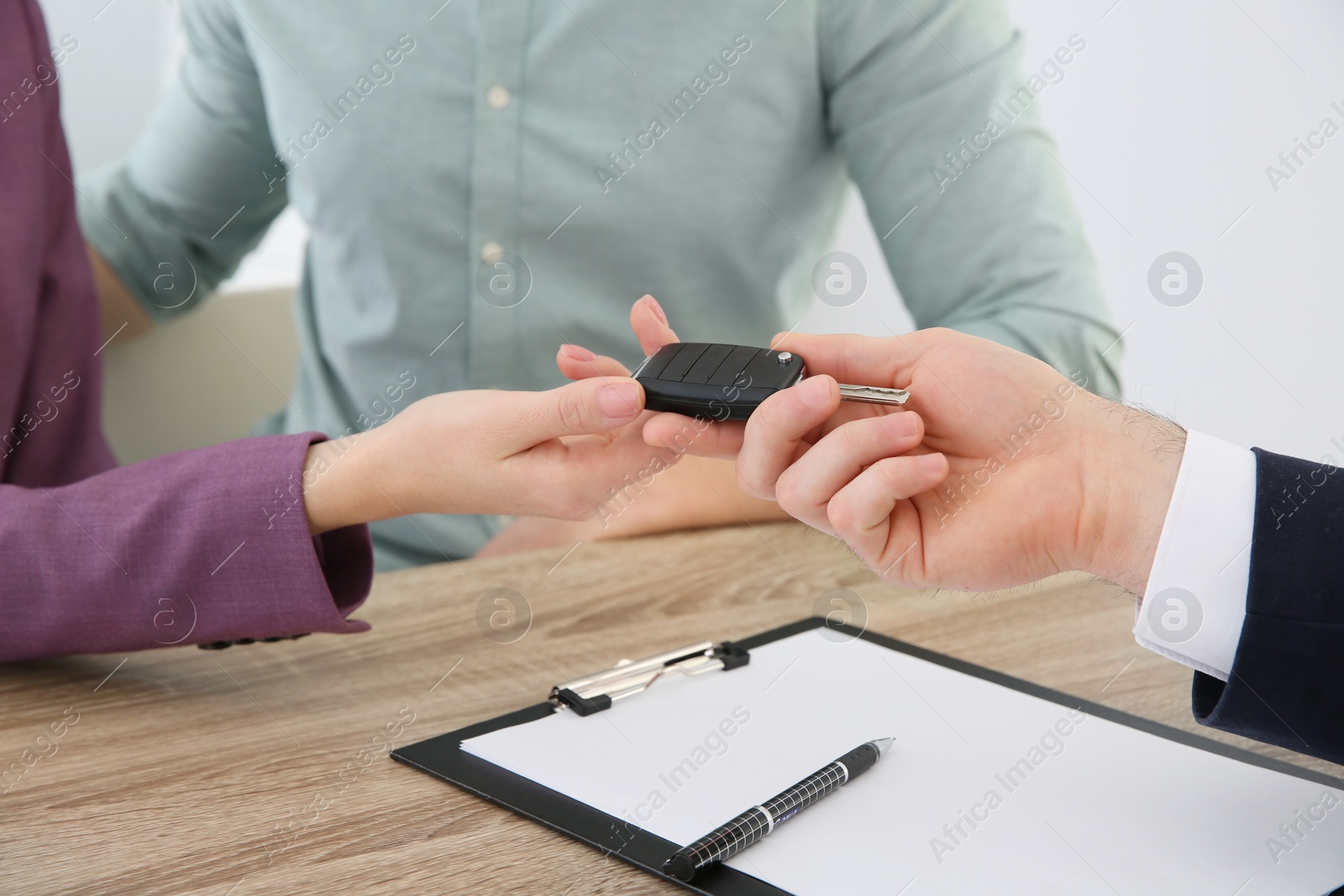 Photo of Salesperson giving car key to young couple in dealership, closeup