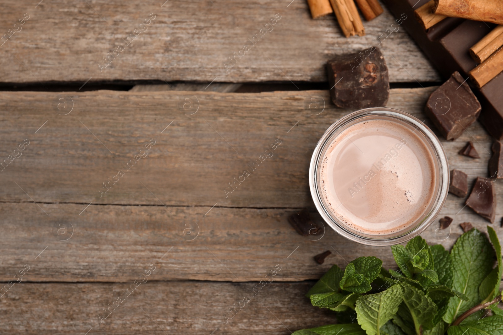 Photo of Glass of delicious hot cocoa with chunks, fresh mint and cinnamon sticks on wooden table, flat lay. Space for text