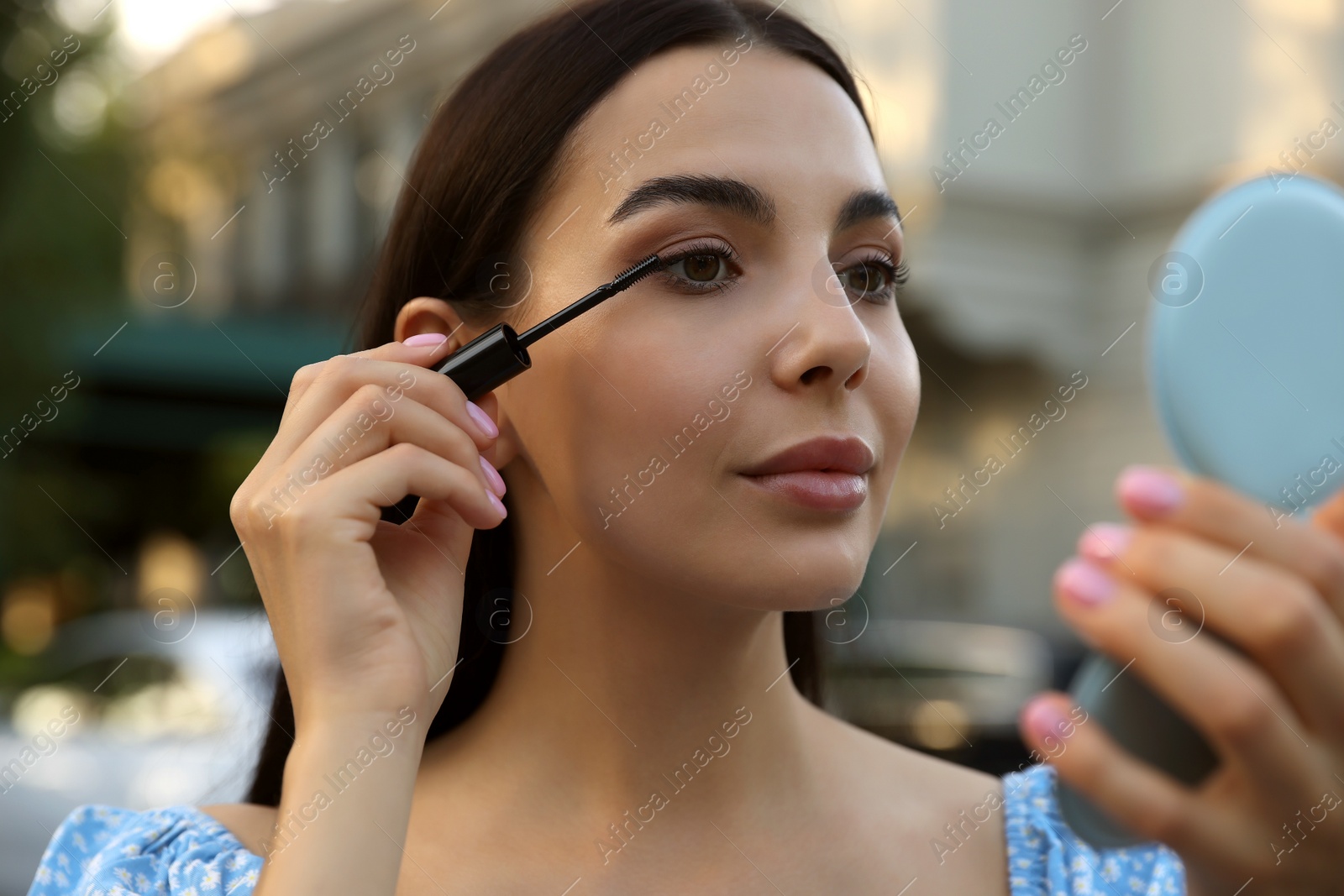 Photo of Beautiful woman with cosmetic pocket mirror applying mascara outdoors, closeup