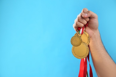 Photo of Man holding golden medals on light blue background, closeup. Space for design