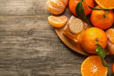 Photo of Bottle of tangerine essential oil and fresh fruits on wooden table, top view. Space for text