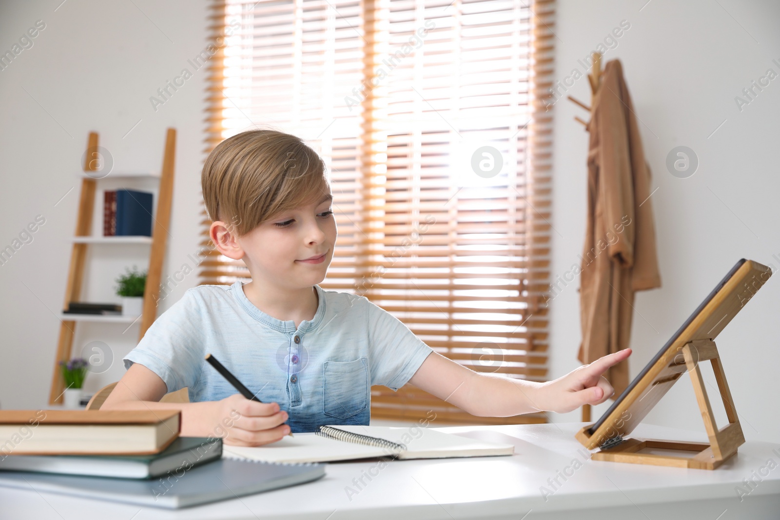 Photo of Boy doing homework with tablet at table indoors