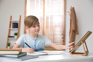Photo of Boy doing homework with tablet at table indoors