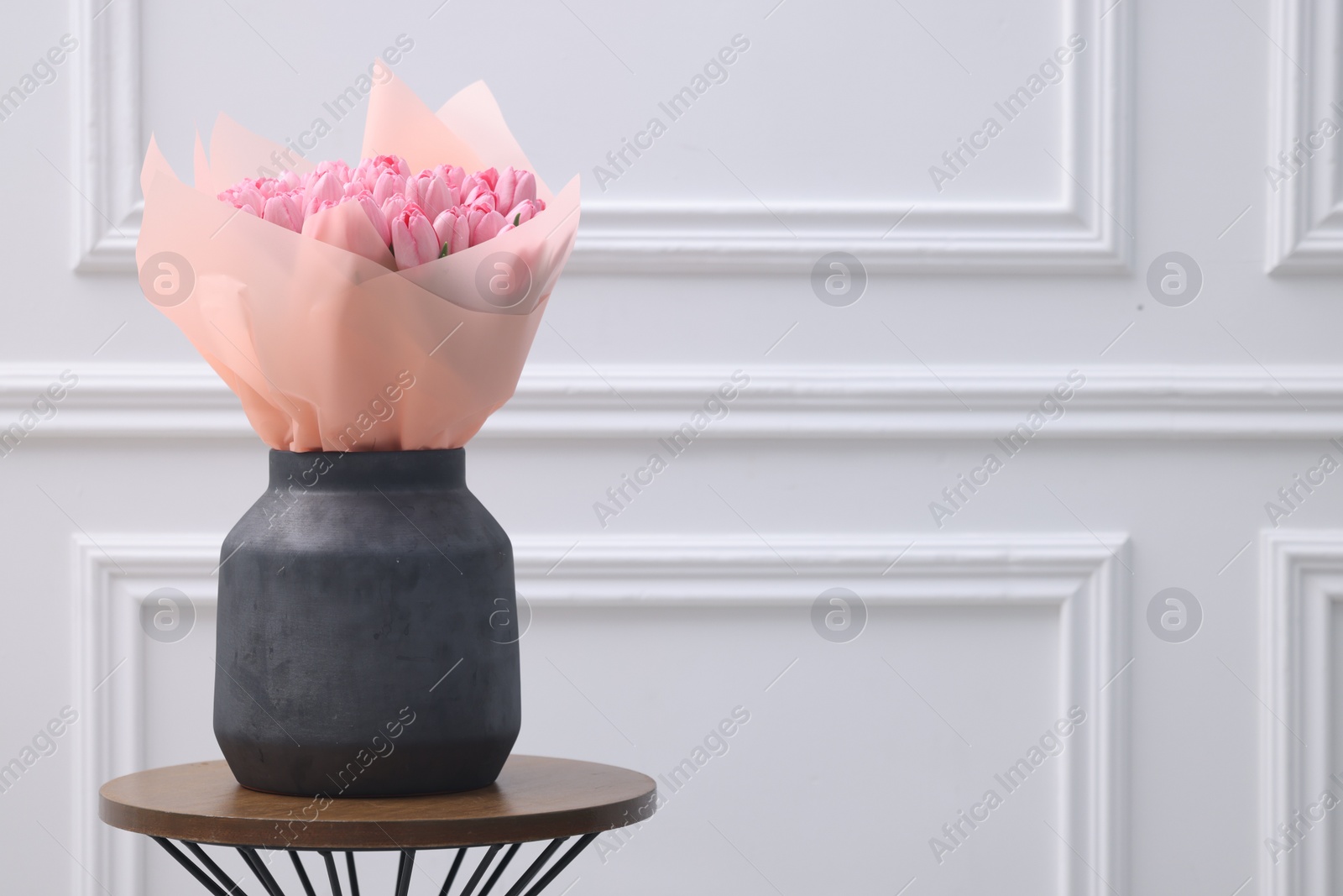 Photo of Bouquet of beautiful pink tulips in vase on wooden table near white wall, space for text