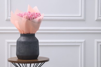 Photo of Bouquet of beautiful pink tulips in vase on wooden table near white wall, space for text