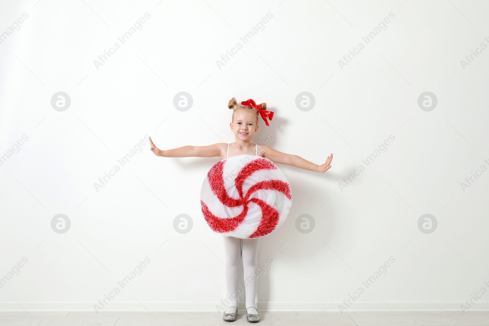 Image of Cute little girl dressed as candy near white wall. Christmas suit