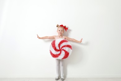 Image of Cute little girl dressed as candy near white wall. Christmas suit