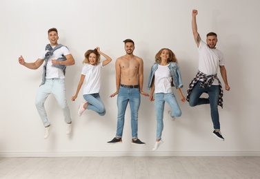 Photo of Group of young people in jeans jumping near light wall