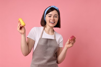Happy confectioner with delicious eclairs on pink background