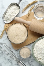 Leaven, flour, ears of wheat, rolling pin, whisk and water on white marble table, flat lay