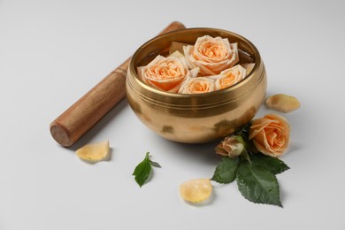 Photo of Tibetan singing bowl with water, mallet and beautiful rose flowers on white background