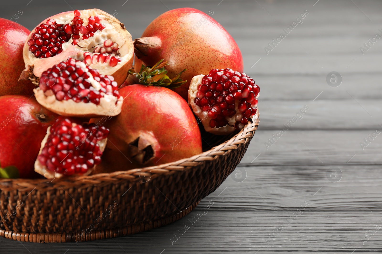 Photo of Delicious ripe pomegranates on grey wooden table, closeup. Space for text
