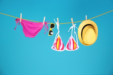 Photo of Beautiful bikini, hat and sunglasses hanging on rope against color background