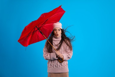 Photo of Emotional woman with broken umbrella caught in gust of wind on light blue background