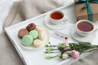 Photo of Tasty breakfast served in bed. Delicious macarons, tea, gift box, flowers and I Love You card on tray