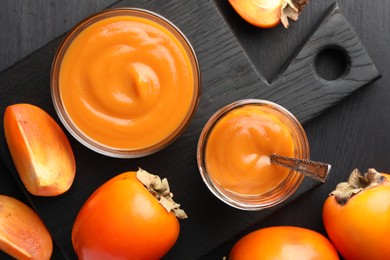 Photo of Delicious persimmon jam and fresh fruits on dark gray wooden table, flat lay