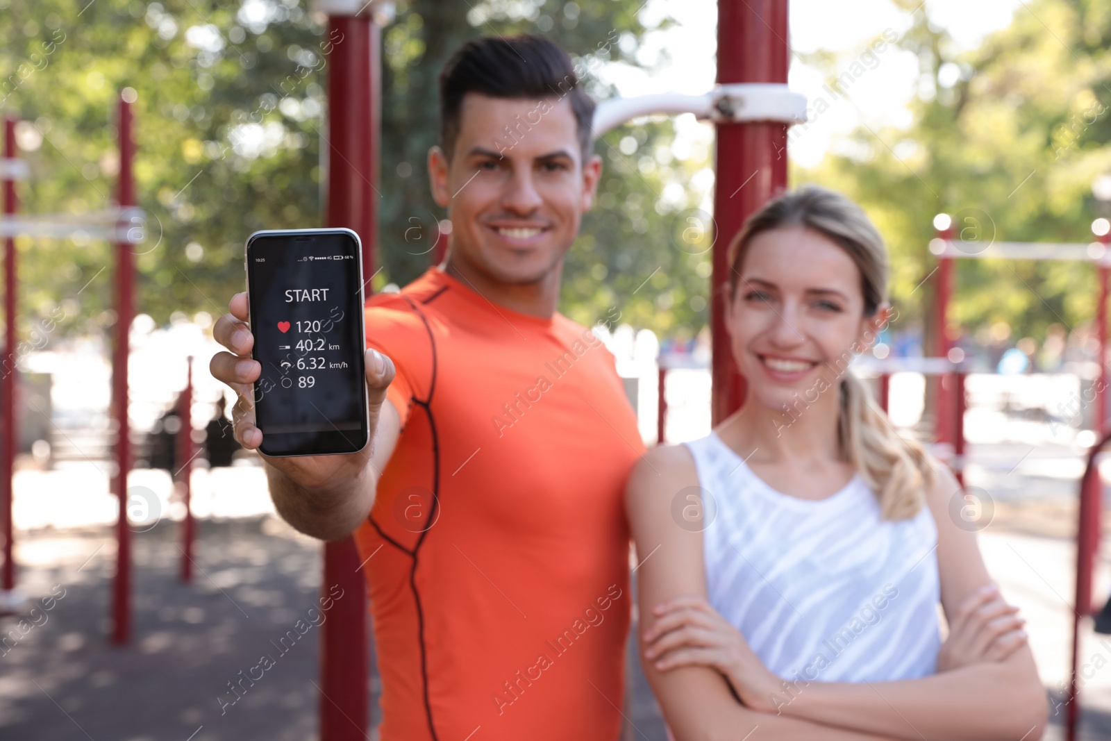 Photo of Couple showing smartphone with fitness app outdoors, focus on device