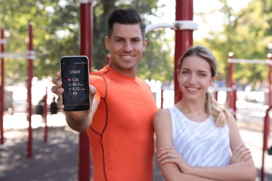 Photo of Couple showing smartphone with fitness app outdoors, focus on device