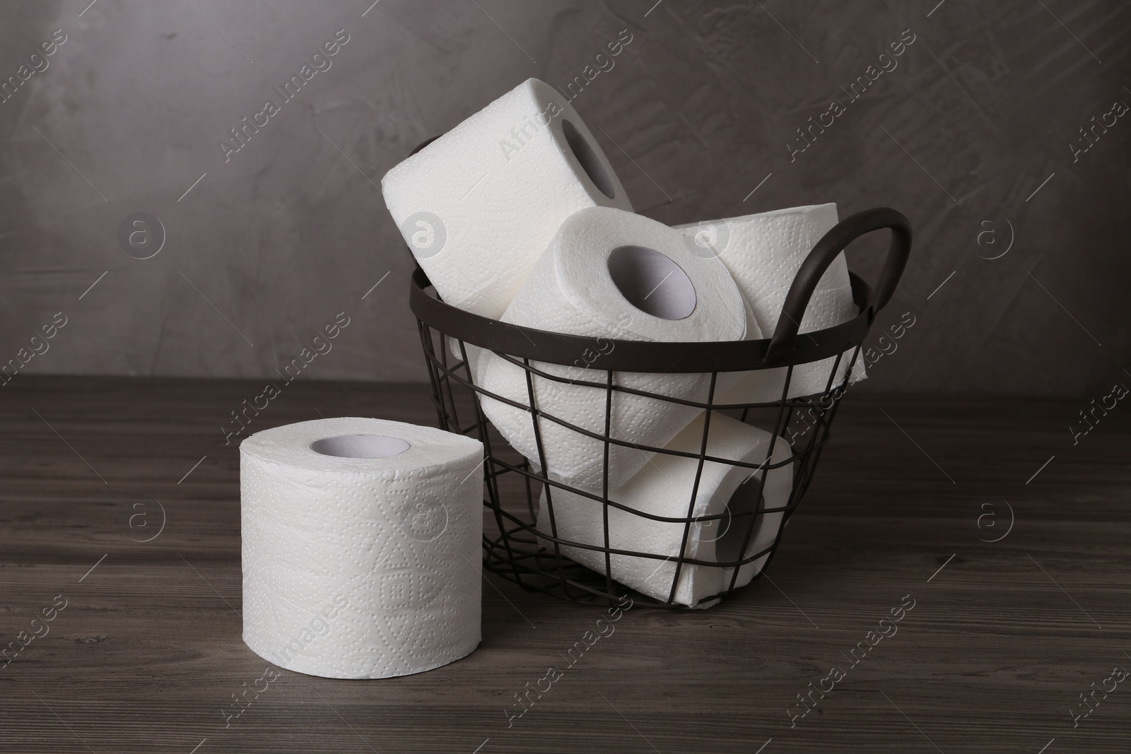 Photo of Soft toilet paper rolls in metal basket on wooden table