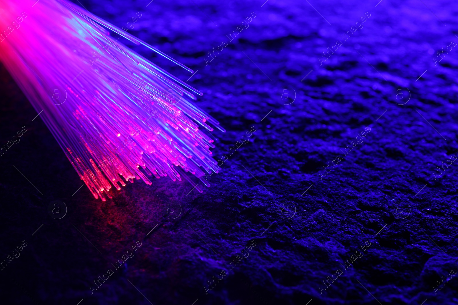 Photo of Optical fiber strands transmitting color light on textured background, closeup. Space for text