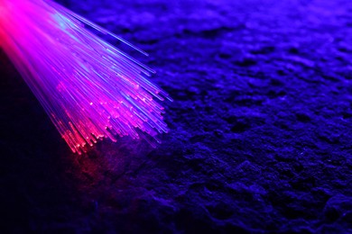 Optical fiber strands transmitting color light on textured background, closeup. Space for text