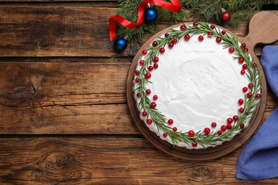 Traditional Christmas cake decorated with rosemary and cranberries on wooden table, flat lay. Space for text