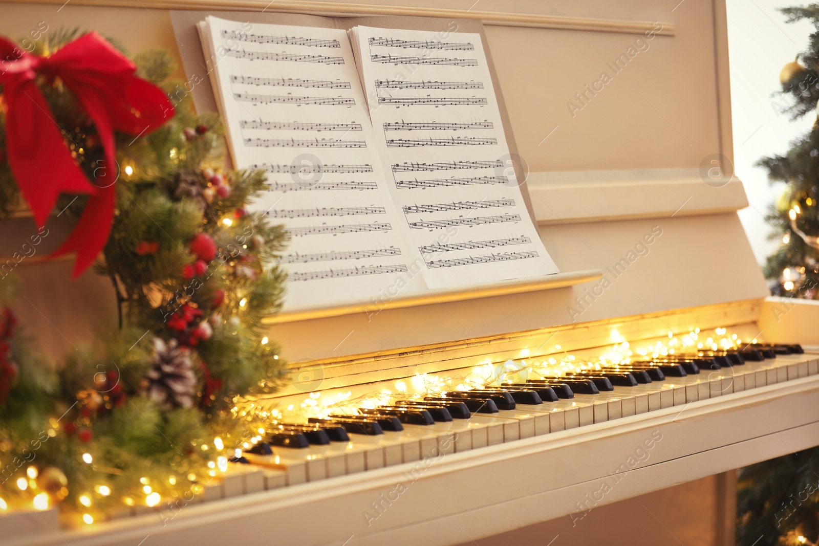 Photo of White piano with fairy lights and note sheets indoors, closeup. Christmas music