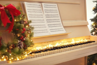 White piano with fairy lights and note sheets indoors, closeup. Christmas music