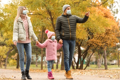 Photo of Family in medical masks walking outdoors on autumn day. Protective measures during coronavirus quarantine