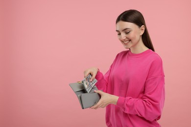 Happy woman putting money into wallet on pink background, space for text