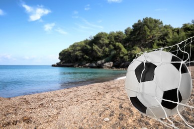 Image of Soccer ball in net on sandy coast near sea. Beach football