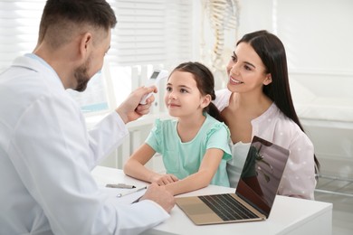 Photo of Mother with daughter visiting pediatrician in hospital. Doctor measuring little girl's temperature