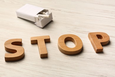 Photo of Pack with cigarettes and word Stop made of letters on white wooden table. No smoking concept