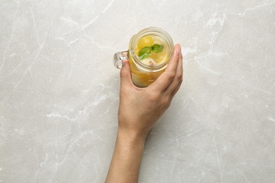 Woman holding Mason jar of melon ball cocktail with mint at light grey marble table, top view