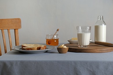 Photo of Milk, honey and bread served for breakfast on grey table indoors