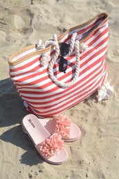 Stylish striped bag with slippers and sunglasses on sandy, above view