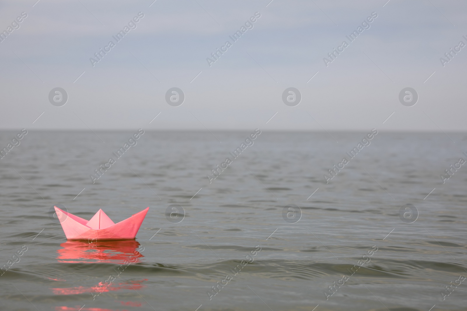 Photo of Pink paper boat on water surface, space for text