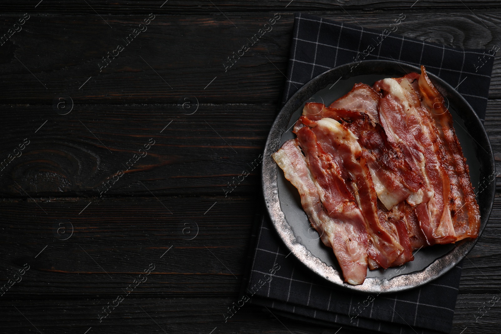 Photo of Slices of tasty fried bacon on black wooden table, top view. Space for text