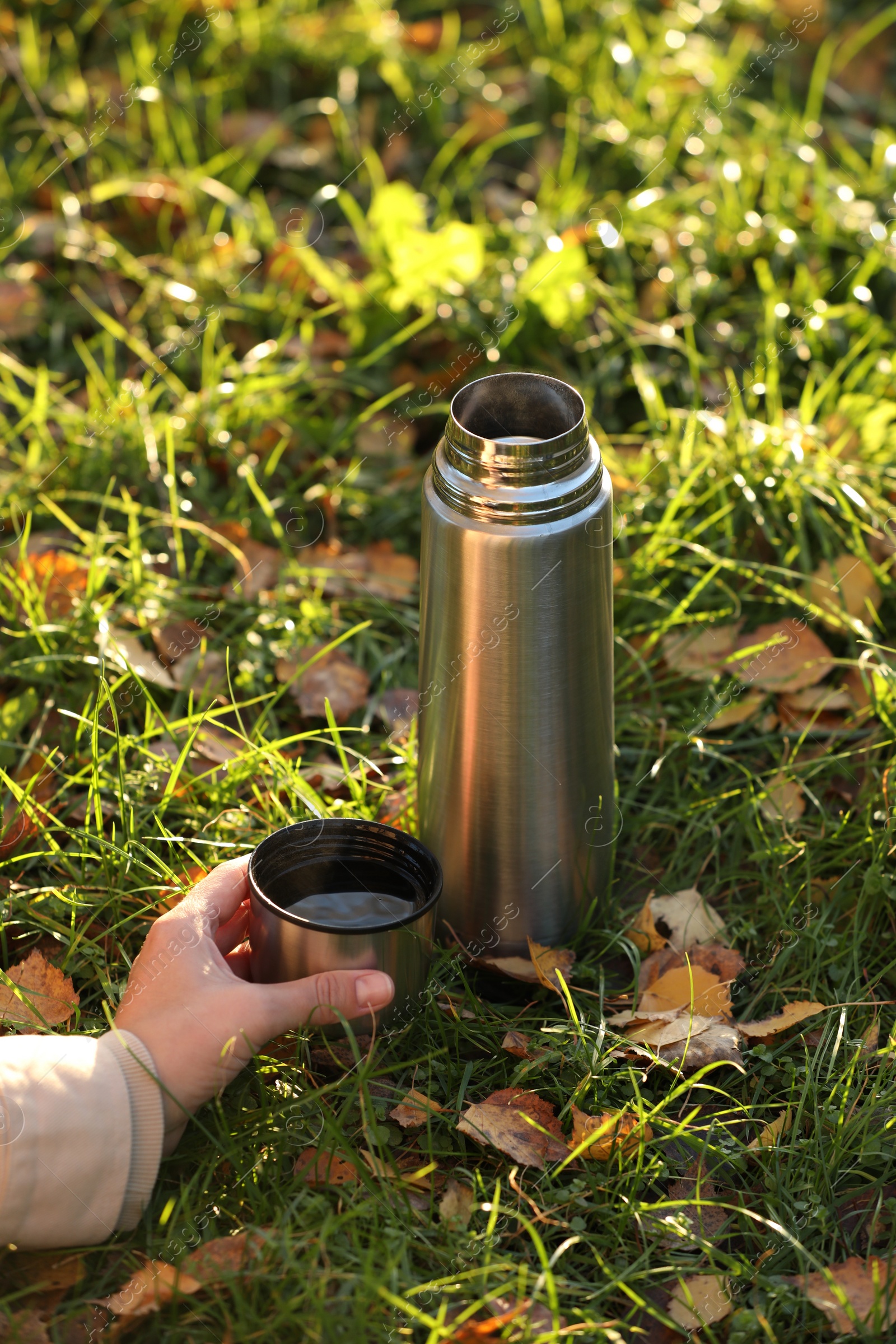 Photo of Woman with thermos and cup lid on green grass in autumn, closeup
