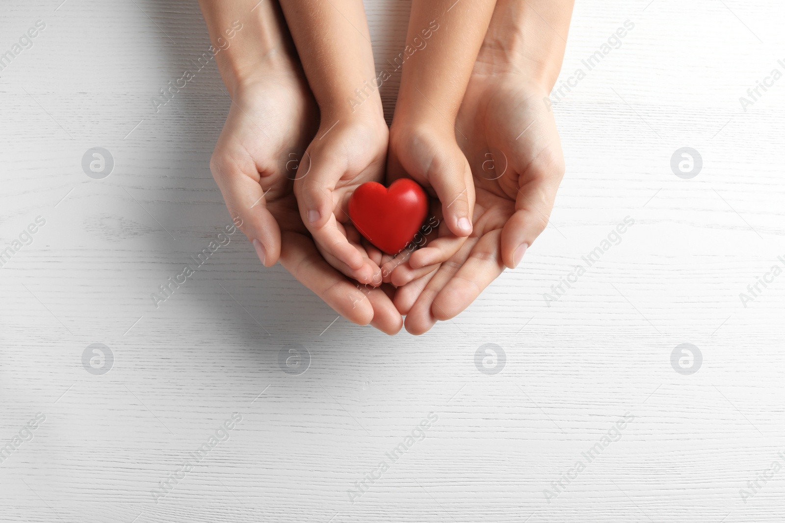 Photo of Family holding small red heart in hands on wooden background