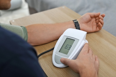 Photo of Man checking blood pressure with sphygmomanometer at table indoors, closeup. Cardiology concept