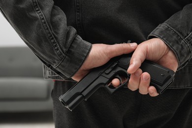 Photo of Man hiding gun behind his back indoors, closeup. Armed robbery