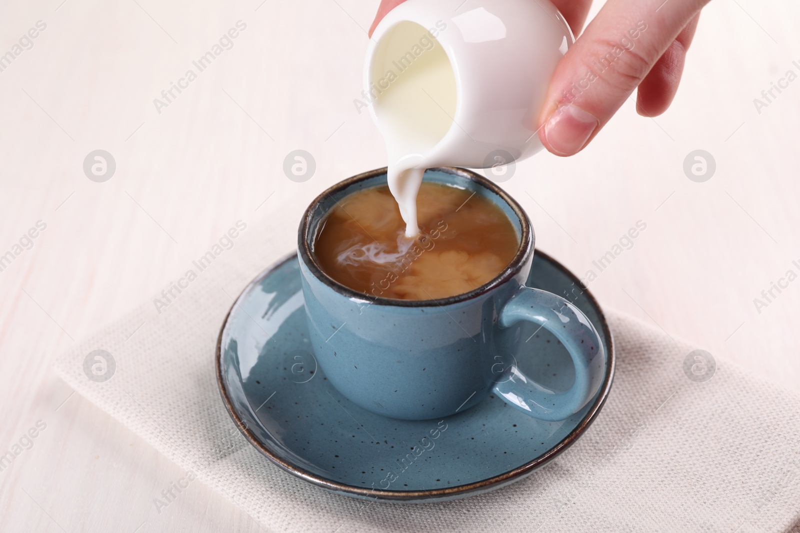 Photo of Woman pouring milk into cup with aromatic coffee at white wooden table, closeup