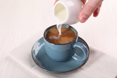 Woman pouring milk into cup with aromatic coffee at white wooden table, closeup