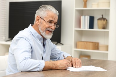 Senior man signing Last Will and Testament at wooden table indoors. Space for text