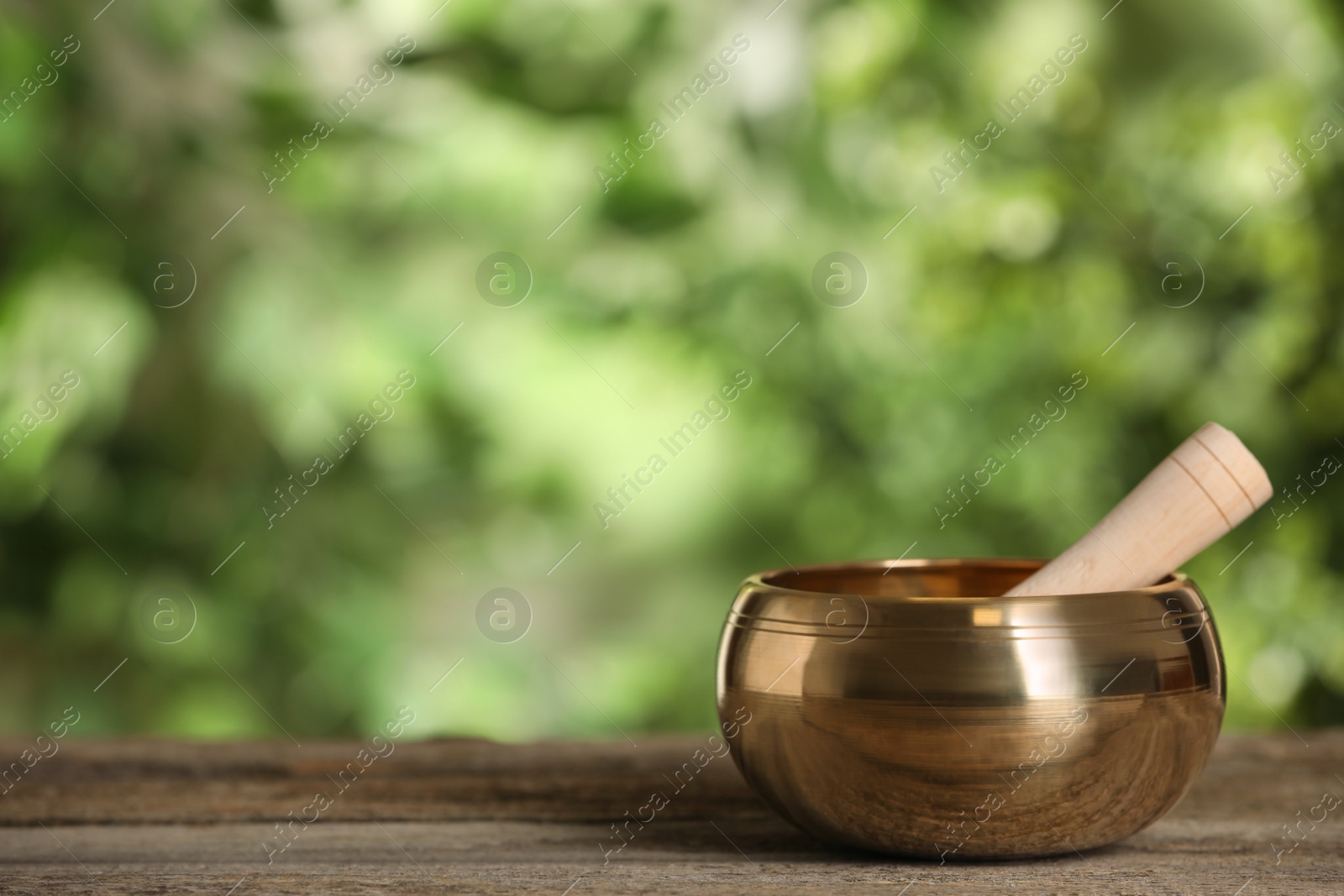 Photo of Golden singing bowl with mallet on wooden table outdoors, space for text