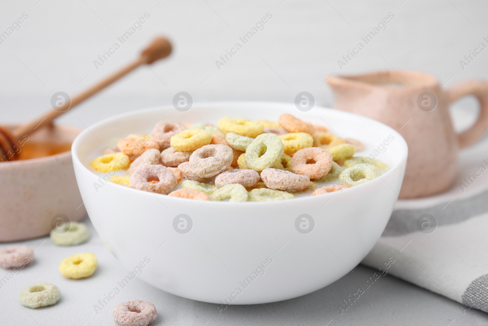 Photo of Cereal rings and milk in bowl on white table, closeup