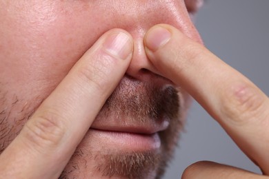 Photo of Man popping pimple on his nose against grey background, closeup