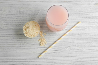 Photo of Protein shake, powder and straw on white wooden table, above view