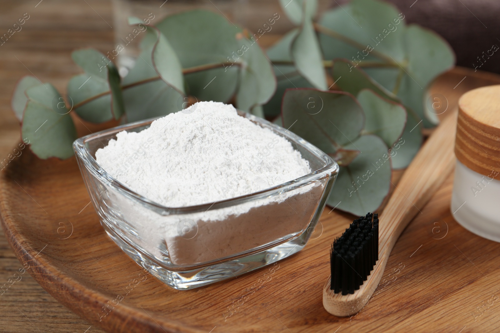 Photo of Tooth powder, brush and eucalyptus on wooden tray, closeup